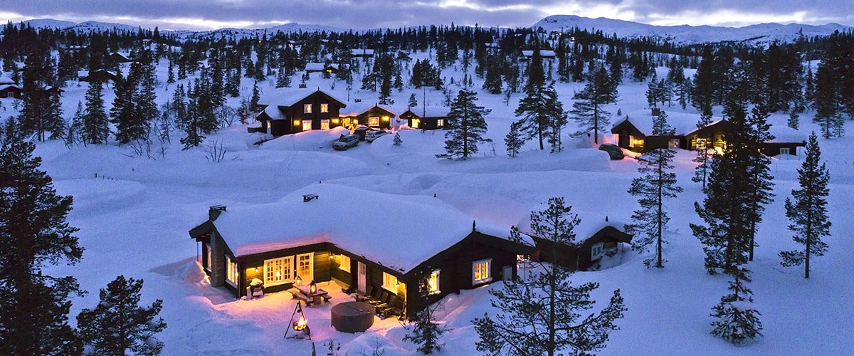 En hytte lyser opp de snødekte fjellomgivelsene i skumringstimen. 