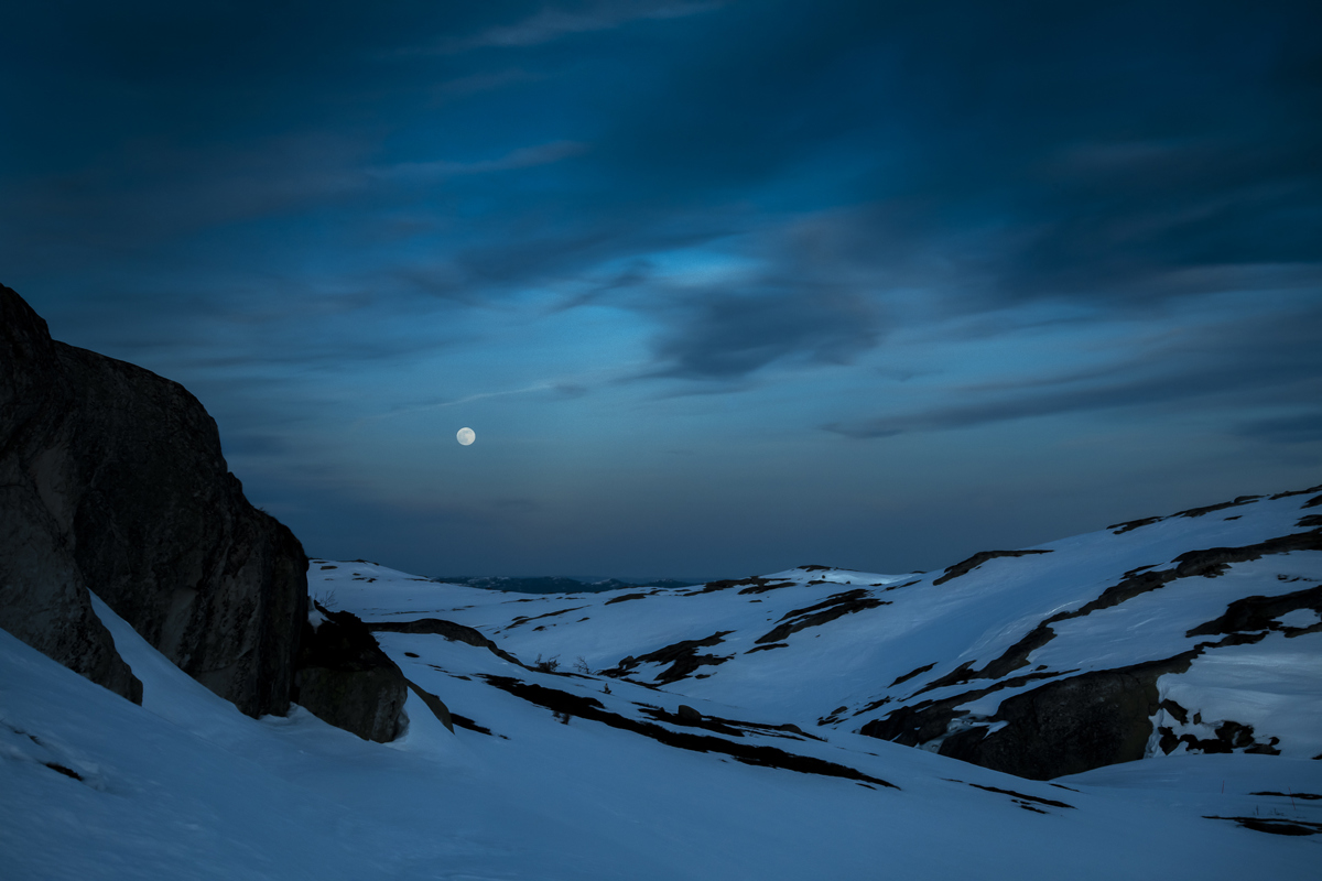 Fullmånen lyser over mørke, snødekte fjelltopper