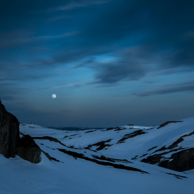 Fullmånen lyser over mørke, snødekte fjelltopper