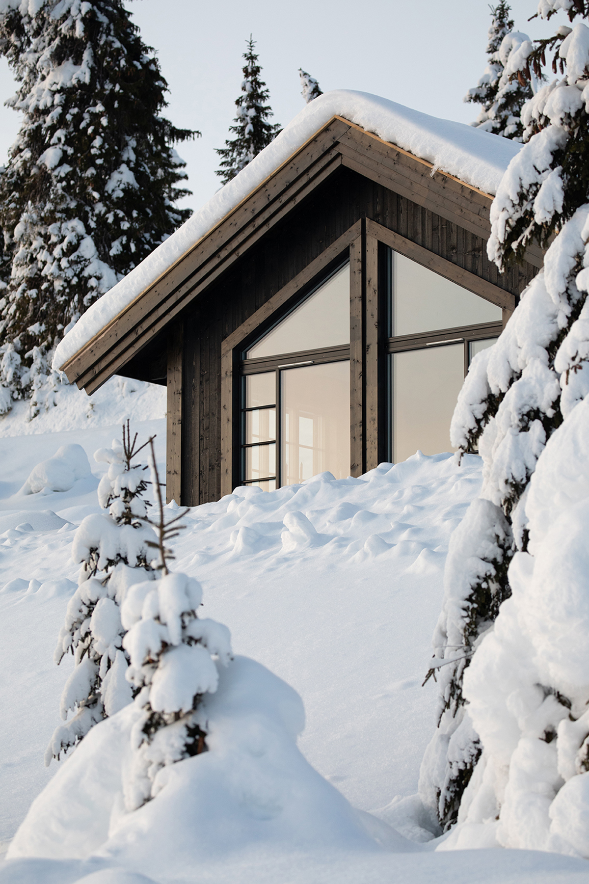 En hytte med store vinduer ligger i et fjellandskap dekket av dyp snø