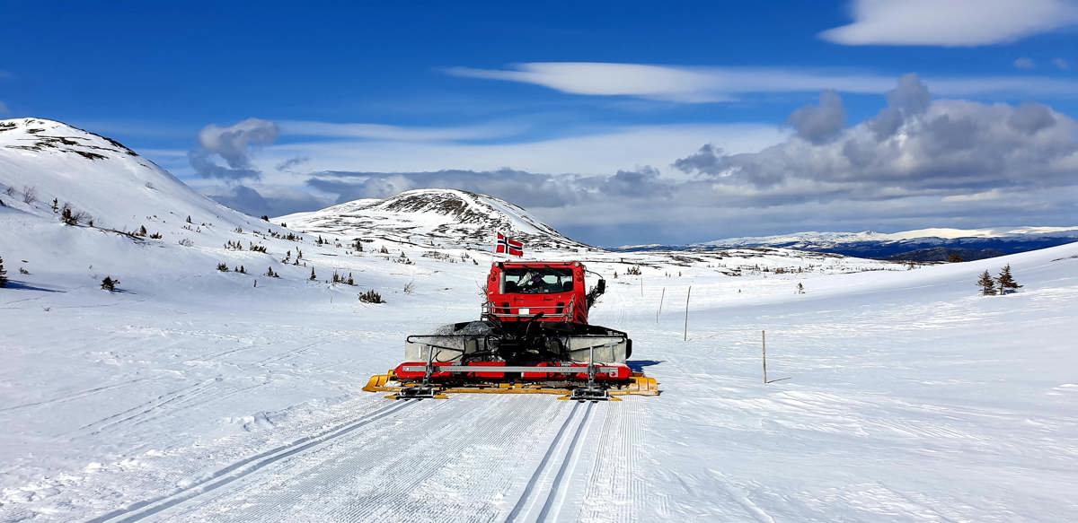 En rød løypemaskin lager nye skiløyper, omkranset av høye fjelltopper