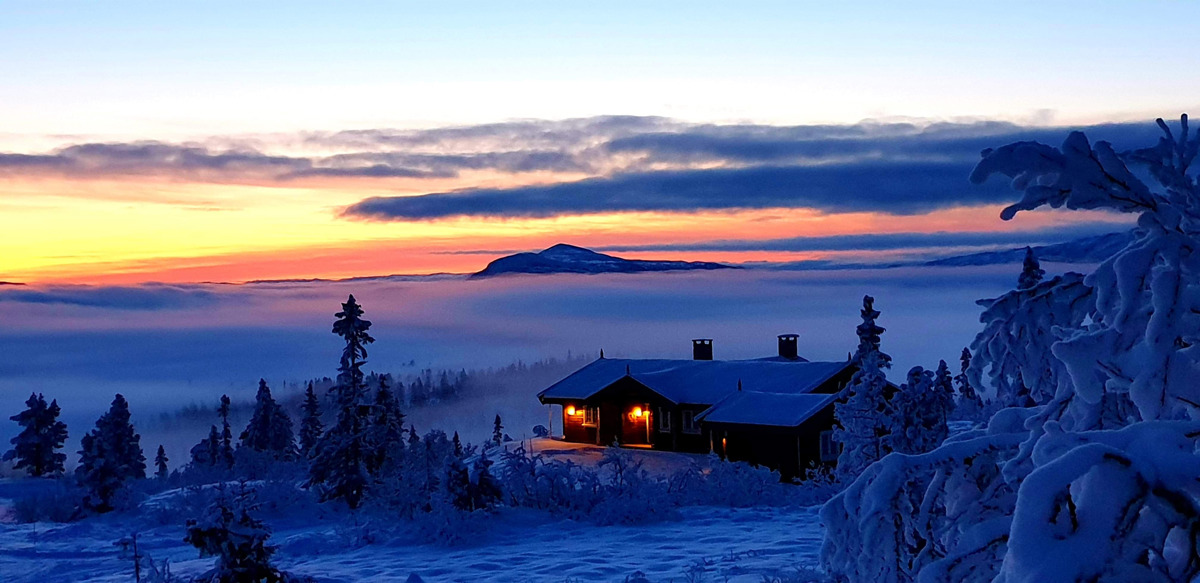 En rød solnedgang lyser over en hytte i et vinterlandskap